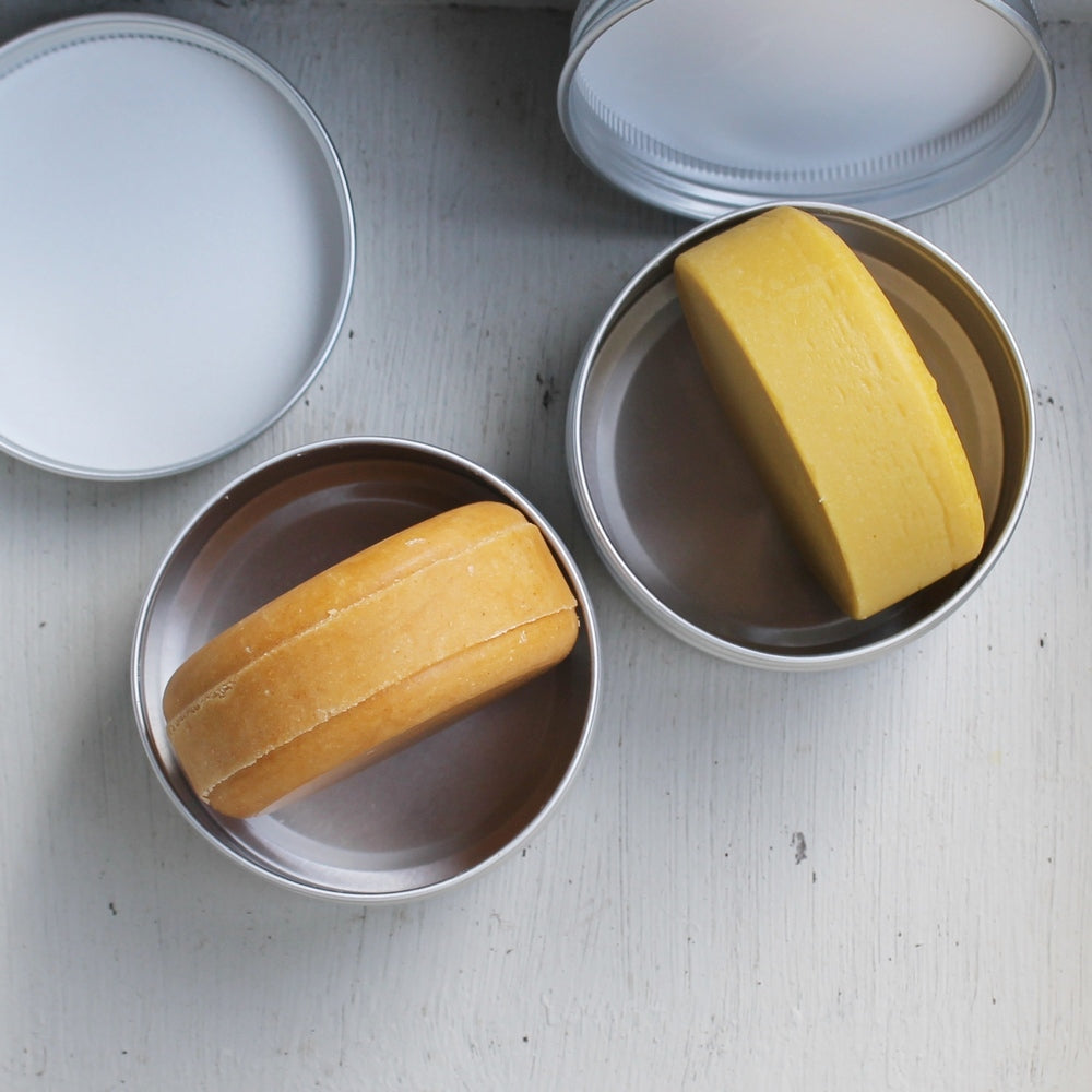 Orange shampoo and orange conditioner bars in tins on white background